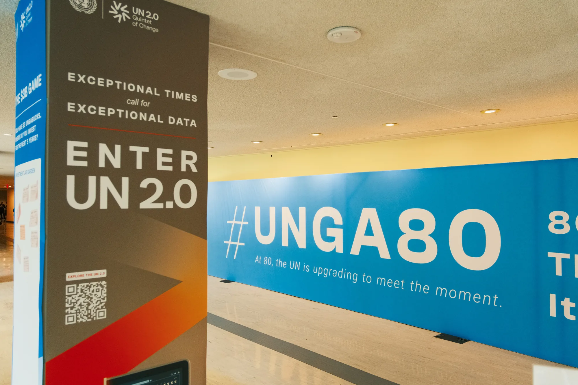 The passage at UN Headquarters: an Enter UN 2.0 pillar standing in the foreground with the blue #UNGA80 wall running down the corridor behind it