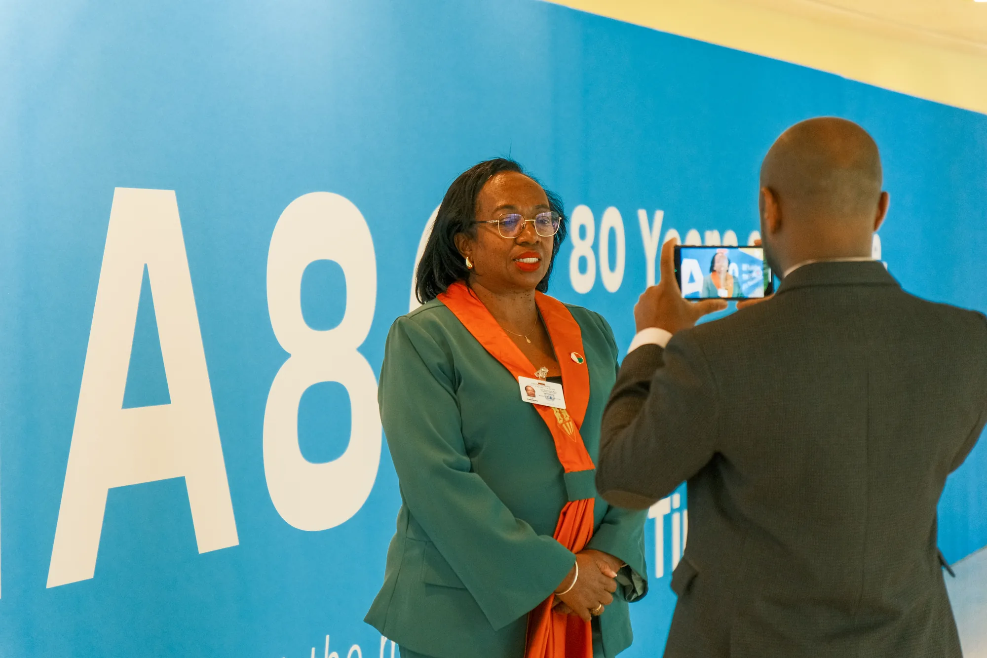 A visitor being photographed in front of the #UNGA80 wall in the passage